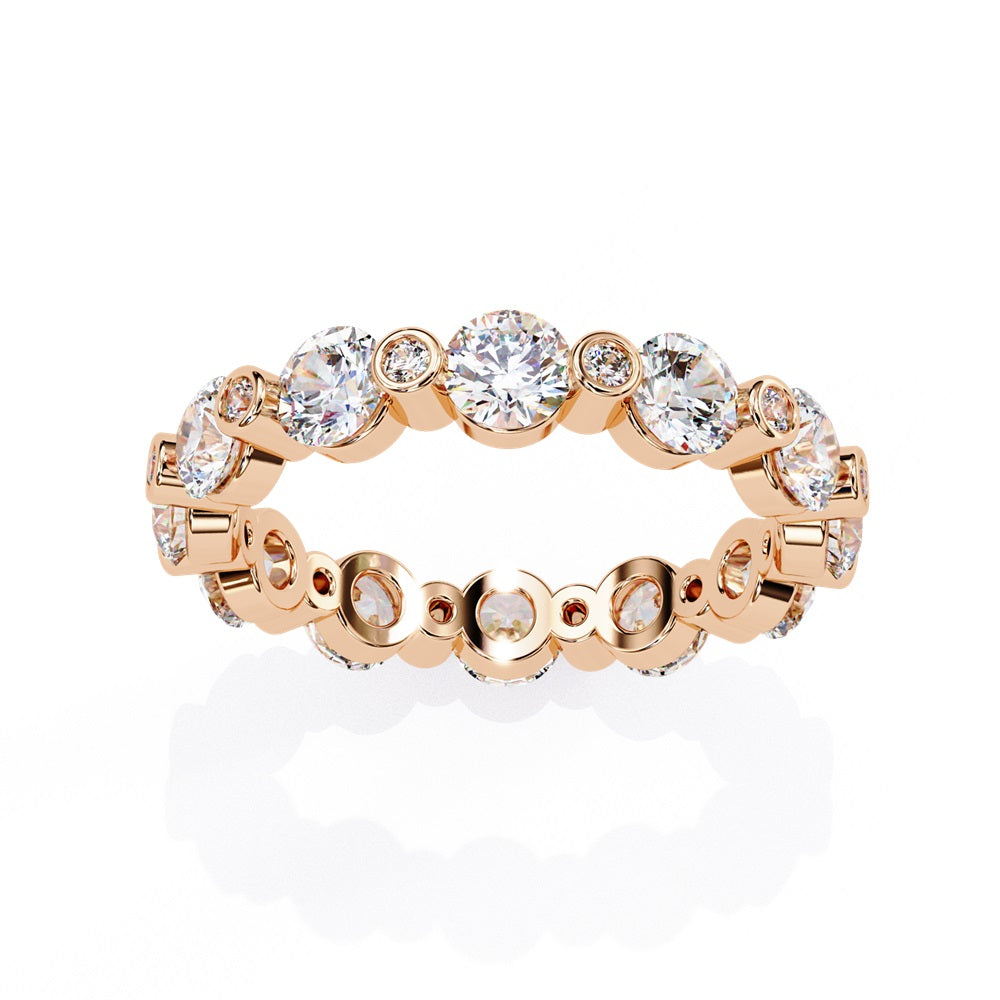 The Niraa Dazzling Diamond Eternity Band, adorned with alternating large and small round diamonds encircling the gold band, embodies luxury through its symmetrical design, showcasing brilliance and elegance in perfect harmony.