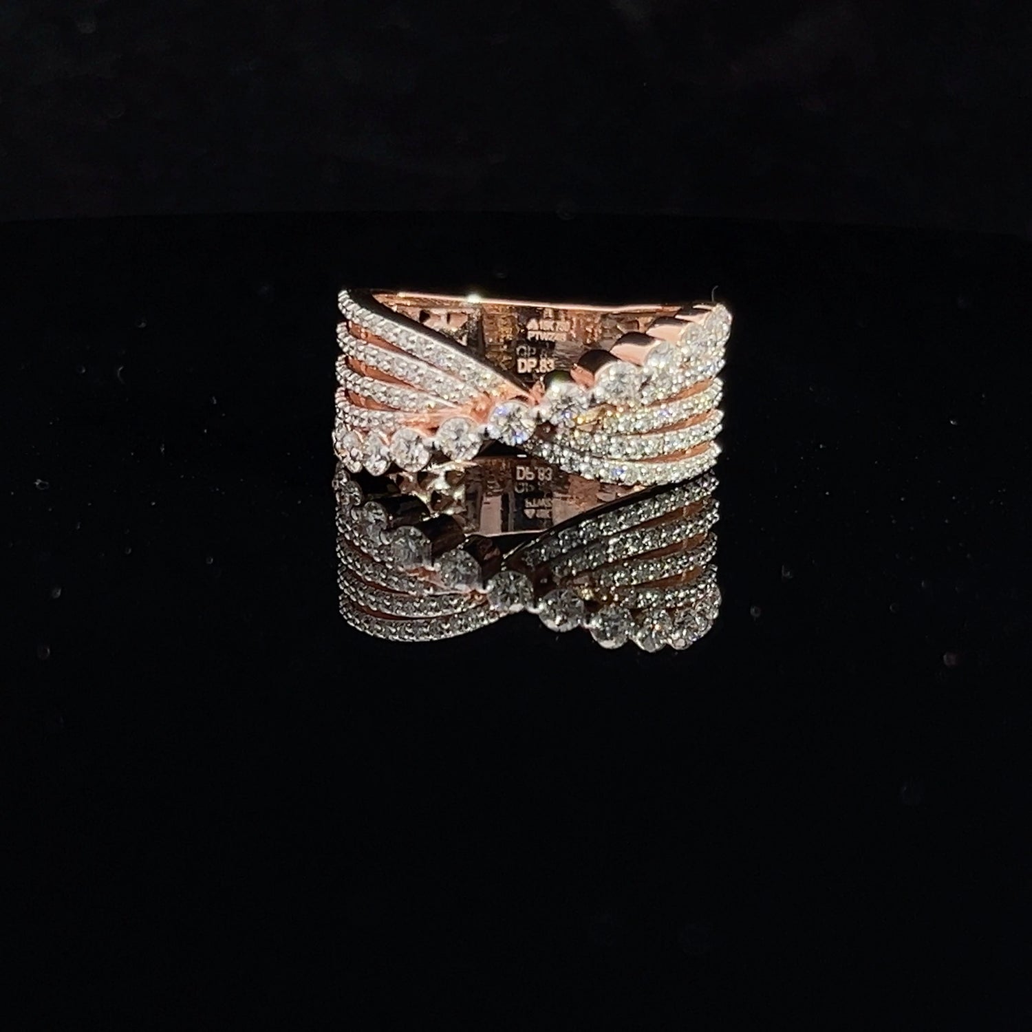 The Trinity Diamond Ladies Ring by Niraa features intricate interwoven bands that glisten on a dark reflective surface. The gold design, adorned with multiple small diamonds, exudes the allure of luxury.