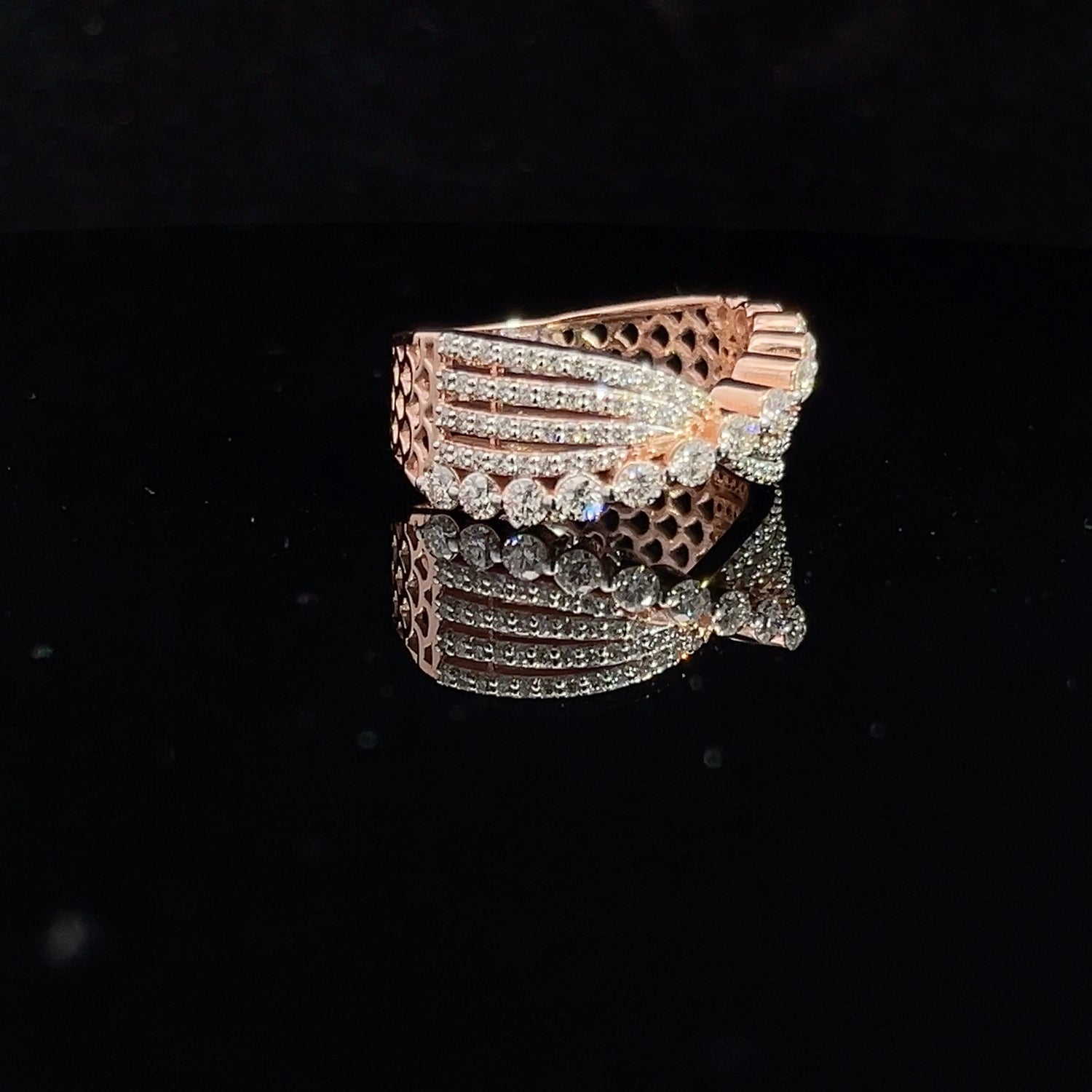 The Trinity Diamond Ladies Ring by Niraa features intricate interwoven bands that glisten on a dark reflective surface. The gold design, adorned with multiple small diamonds, exudes the allure of luxury.